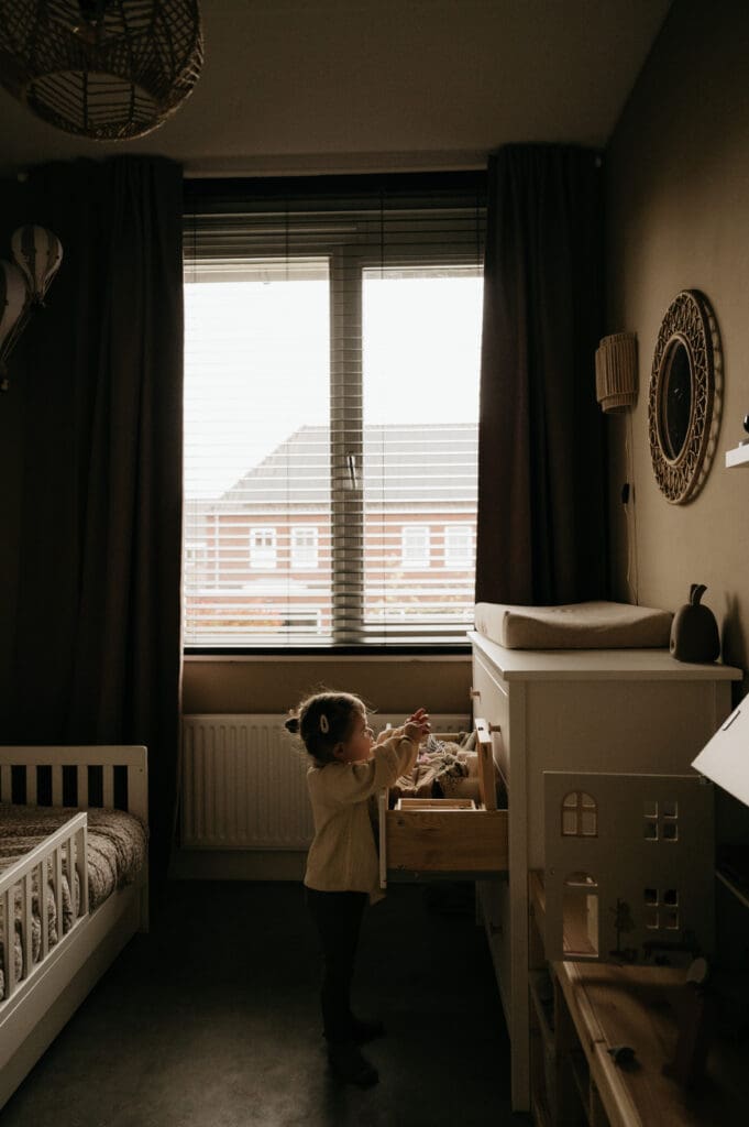 achte en sfeervolle documentaire fotografie van een kind dat rustig bij het raam zit binnenshuis.
