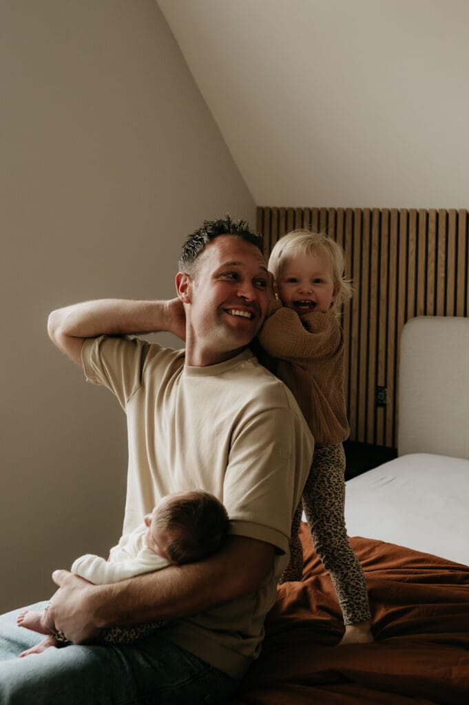 Fotografie op kinderhoogte van een lachende papa die met zijn kind knuffelt en speelt op het ouderbed.